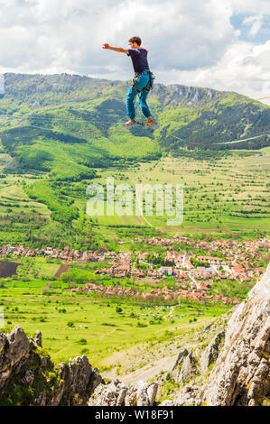 Junger Mann auf einem Highline oben scharf gezackten Klippen. Slackline in den Bergen mit wunderschönen grünen Hänge und flauschige Wolken im Hintergrund Stockfoto