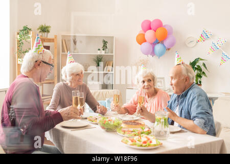 Vier älteren Freunde mit Champagner sitzend Durch festliche Tafel während home Geburtstagsfeier Stockfoto
