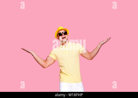 Positive männliche im trendigen Outfit, Hut und Sonnenbrille mit Händen posiert auf rosa Hintergrund im Studio. Isolieren Stockfoto