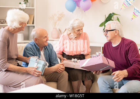 Vier zeitgenössische Senioren Geschenke, miteinander sprechen und während der Ferien zu Hause feiern. Stockfoto