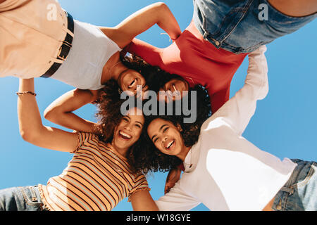 Low Angle View von Happy weibliche Freunde mit lockigem Haar stehen im Kreis und auf Kamera. Mädchen in eine Hürde nach unten schauen und Lachen. Stockfoto