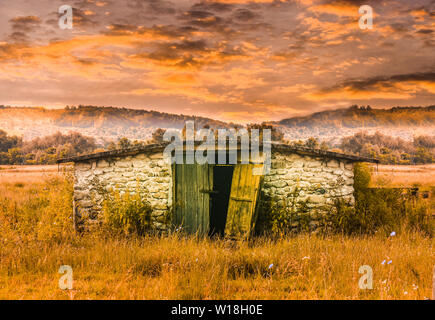 Scheune Gebäude in der Rasenfläche bei Sonnenuntergang. Alten, Verlassenen in Märchen Szene beleuchten. Styled Foto mit der Landschaft in Rumänien. Stockfoto