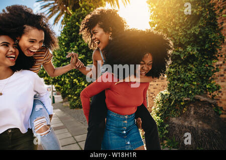 Glückliche junge Frauen sich auf der Straße der Stadt. Gruppe von multi-ethnischen Freunde genießen im Freien. Frauen huckepack ihre Freunde. Stockfoto