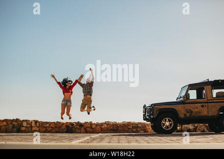 Junger Mann und Frau springen draußen vor dem Auto. Paar in eine große Zeit auf Reise. Stockfoto