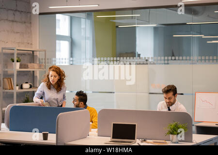 Gruppe von Unternehmen Mitarbeiter am Tisch sitzen im Büro und die Lösung von Problemen: Curly blonde Dame erklärt Projektidee zu Kollegen, während Ihre col Stockfoto