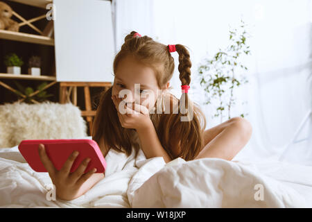 Mädchen über verschiedene Geräte zu Hause. Kleines Modell in Ihrem Zimmer mit Smartphone sitzen und selfie oder über Videochat mit ihren Freunden. Konzept der Interaktion von Kindern und moderne Technologien. Stockfoto