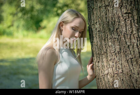 Junge Frau im Wald sitzt auf einen umgestürzten Baum mit Löwenzahn auf ihre Hand. Die Einheit mit der Natur. Stockfoto