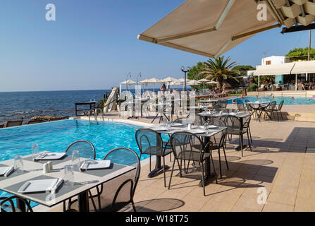 Kreta, Griechenland. Juni 2019. Restaurant am Pool Tisch und Stühlen mit Blick auf die Bucht von Chania Norden von Kreta. Stockfoto