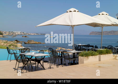 Kreta, Griechenland. Juni 2019. Restaurant am Pool Tisch und Stühlen mit Blick auf die Bucht von Chania Norden von Kreta. Stockfoto