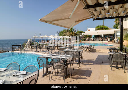 Kreta, Griechenland. Juni 2019. Restaurant am Pool Tisch und Stühlen mit Blick auf die Bucht von Chania Norden von Kreta. Stockfoto