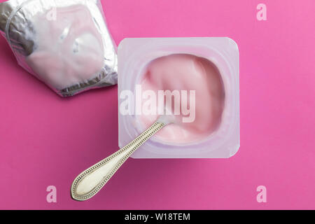 Gesunde strawberry rosa Joghurt mit Fruchtgeschmack und Löffel in kleinen Plastikbecher auf rosa Hintergrund mit Folie Deckel isoliert - Kopieren Platz top Foto anzeigen Stockfoto
