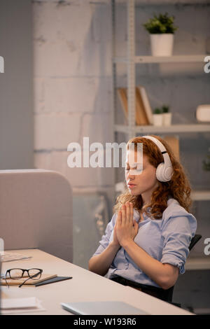 Ruhe konzentriert junge Frau im Kopfhörer bei Tisch sitzen im Büro und betend für den Vertrieb des neuen Produkts Stockfoto