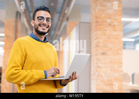 Portrait von fröhlichen stattlichen Mixed Race Office Mann mit Bart im Dachboden und mit tragbaren Computer Stockfoto