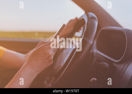 Gefährliche sms während der Fahrt Verhalten, in der Nähe von weiblichen Händen mit Handy und Betrieb von Kraftfahrzeugen auf der Straße durch die Landschaft, selecti Stockfoto