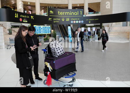 Chinesisches Paar mit Gepäck im Terminal 1, das auf Mobiltelefone am Flughafen Lissabon in Portugal Europa schaut EU KATHY DEWITT Stockfoto