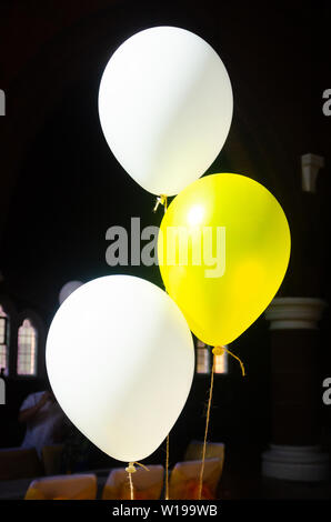 Heluim gefüllt Latex Luftballons in Gelb und Weiß mit String als Dekorationen bei einer Feier verwendet gebunden. Stockfoto