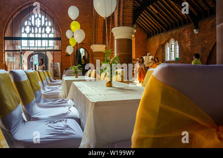 Tische und Stühle in einer Kirche Halle, mit Helium gefüllte Ballons und gelben Bändern bereit für eine Party, Empfang oder Feier eingerichtet Stockfoto