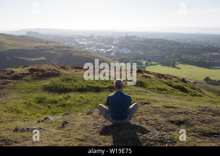 Ein Mann verbringt, ruhige, persönliche Zeit mit Blick auf die Stadt Edinburgh vom Holyrood Park, dem am 26. Juni 2019 in Edinburgh, Schottland. Stockfoto