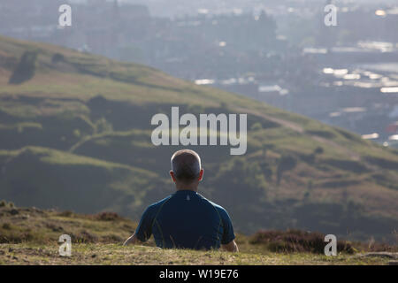 Ein Mann verbringt, ruhige, persönliche Zeit mit Blick auf die Stadt Edinburgh vom Holyrood Park, dem am 26. Juni 2019 in Edinburgh, Schottland. Stockfoto