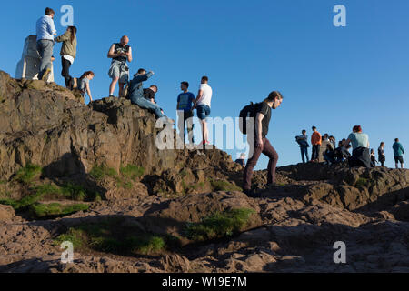 Wanderer geniessen Sie den Sommer Abend Sonnenschein auf dem Gipfel des Arthur's Seat in Holyrood Park, mit Blick auf die Stadt Edinburgh, am 26. Juni 2019 in Edinburgh, Schottland. Arthur's Seat ist ein erloschener Vulkan, der Hauptgipfel der Gruppe von Hügeln in Edinburgh, Schottland, welche Form die meisten Holyrood Park, von Robert Louis Stevenson als "ein Hügel für Größe beschrieben, ein Berg im Rahmen ihrer bold Design" betrachtet wird. Der Hügel erhebt sich über der Stadt auf einer Höhe von 250.5 m (822 ft), einen ausgezeichneten Panoramablick über die Stadt und darüber hinaus. Stockfoto