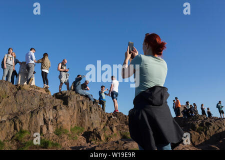 Wanderer geniessen Sie den Sommer Abend Sonnenschein auf dem Gipfel des Arthur's Seat in Holyrood Park, mit Blick auf die Stadt Edinburgh, am 26. Juni 2019 in Edinburgh, Schottland. Arthur's Seat ist ein erloschener Vulkan, der Hauptgipfel der Gruppe von Hügeln in Edinburgh, Schottland, welche Form die meisten Holyrood Park, von Robert Louis Stevenson als "ein Hügel für Größe beschrieben, ein Berg im Rahmen ihrer bold Design" betrachtet wird. Der Hügel erhebt sich über der Stadt auf einer Höhe von 250.5 m (822 ft), einen ausgezeichneten Panoramablick über die Stadt und darüber hinaus. Stockfoto