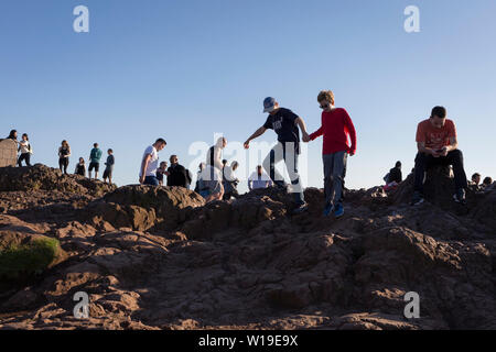 Wanderer geniessen Sie den Sommer Abend Sonnenschein auf dem Gipfel des Arthur's Seat in Holyrood Park, mit Blick auf die Stadt Edinburgh, am 26. Juni 2019 in Edinburgh, Schottland. Arthur's Seat ist ein erloschener Vulkan, der Hauptgipfel der Gruppe von Hügeln in Edinburgh, Schottland, welche Form die meisten Holyrood Park, von Robert Louis Stevenson als "ein Hügel für Größe beschrieben, ein Berg im Rahmen ihrer bold Design" betrachtet wird. Der Hügel erhebt sich über der Stadt auf einer Höhe von 250.5 m (822 ft), einen ausgezeichneten Panoramablick über die Stadt und darüber hinaus. Stockfoto