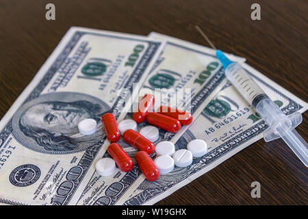 Geld und Pillen mit Drogen und einer Spritze auf der medizinischen Tabelle Stockfoto