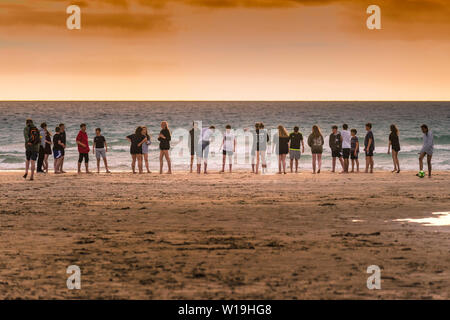 Eine Gruppe von Jugendlichen heraus hängen auf den Fistral Beach in einer dramatischen Sonnenuntergang in Newquay in Cornwall. Stockfoto