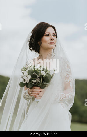 Braut holding Wedding Bouquet. Junge Braut tragen Elegantes Brautkleid Suchen in die Ferne. Stockfoto