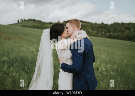 Braut und Bräutigam küssen am Tag ihrer Hochzeit. Frisch verheiratete Ehepaar in Liebe umarmen in der freien Natur. Stockfoto