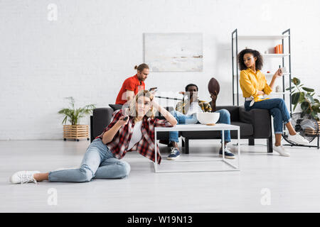 Selektiver Fokus der unzufrieden liegende Frau am Tisch und Holding remore Steuerung im Wohnzimmer Stockfoto