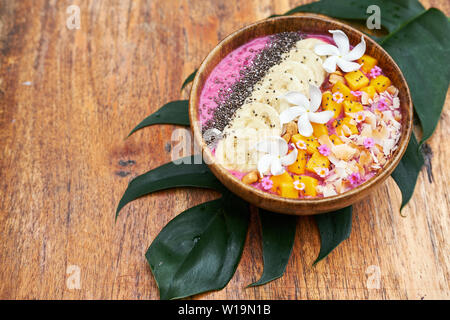 Tropisches Frühstück Fruit Smoothie Schüssel. Gesunde Mango und Banane essen in hölzerne Schüssel auf dem Tisch. Exotische Vegane frische Getränk mit Blumendekoration. Mornin Stockfoto