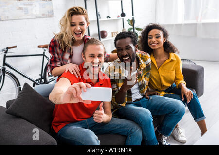 Selektiver Fokus der lächelnden multikulturellen Freunde sitzen auf der Couch und unter selfie zu Hause Stockfoto