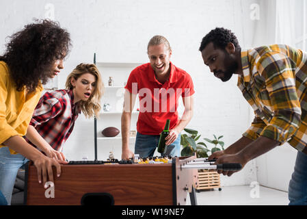 Vier aufgeregt multikulturellen Freunde spielen Tischfußball im Wohnzimmer zu Hause Stockfoto
