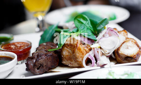 Stücke von Fleisch mit Zwiebeln auf Spieße Kebab. Mit Sauce auf einem weißen Teller servieren. Stockfoto