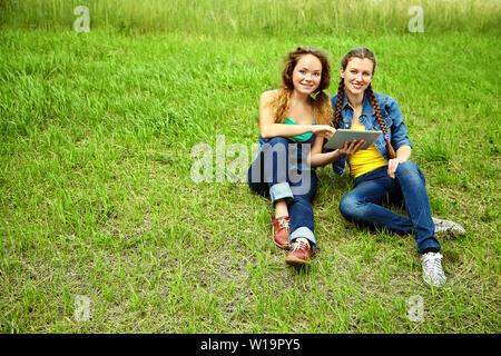 zwei Freunde mit Tablet-PC sitzen auf dem Rasen im Sommerpark. Jugend-lifestyle Stockfoto