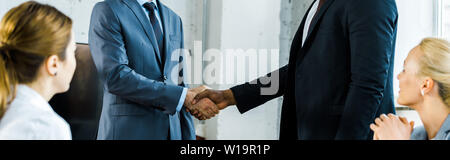 Panorama-aufnahme des multikulturellen Geschäftsleute Händeschütteln in der Nähe von Kollegen im Büro Stockfoto