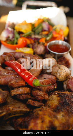 Gemischte gegrillte Fleischplatte. Sortierte lecker Gegrilltes Fleisch mit Gemüse. Gemischte gegrilltes Fleisch mit Pfeffer Soße und Gemüse. Stockfoto