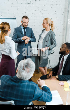 Business Coach schaut auf eine Wand in der Nähe der multikulturelle Mitarbeiter und schwanger blonde Frau Stockfoto