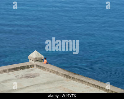 Frau in orange Top saß auf Sea Wall an einem ruhigen Atlantik suchen Stockfoto