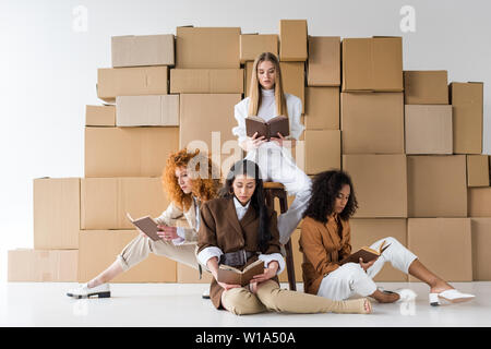 Multikulturelle Mädchen sitzt in der Nähe der Boxen und Bücher lesen auf Weiß Stockfoto