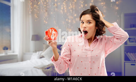 Junge Frau im Pyjama mit Wecker schockiert Stockfoto