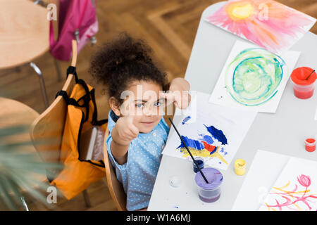 Ansicht von oben von niedlichen afrikanische amerikanische Kid zeigt mit Finger in der Nähe von Papier mit der Malerei Stockfoto