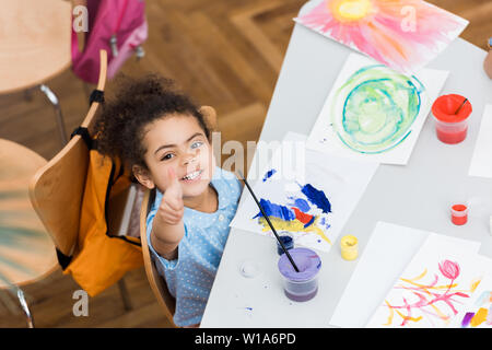 Ansicht von oben von Happy african american Kind zeigt mit dem Finger in der Nähe von Papier mit der Malerei Stockfoto