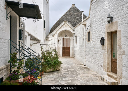 Gemütlicher Innenhof mit vielen bunten Pflanzen in Töpfen zwischen Trulli in Alberobello Stadt in Italien. Es gibt vintage Laternen und Postfächer auf facad Stockfoto