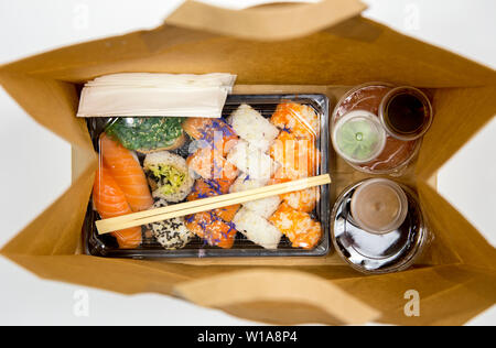 Sushi Konzept zu gehen. Blick von oben auf die Kästchen mit Sushi zum Mitnehmen Brötchen und verschiedene Sauce Cups in der braunen Papiertüte. Auf weißen, Studio shot isoliert. Stockfoto