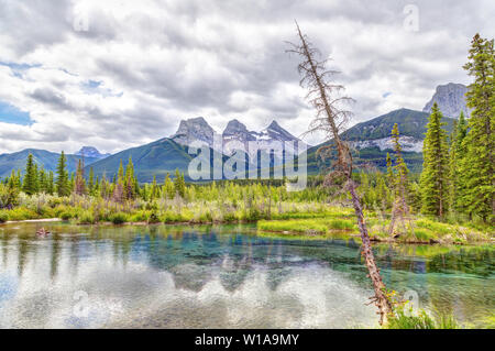 Die Canmore berühmten Three Sisters Berggipfel und deren Reflexionen auf dem Bow River im südlichen Banff Spektrum der Kanadischen Rockies an einem bewölkten S Stockfoto