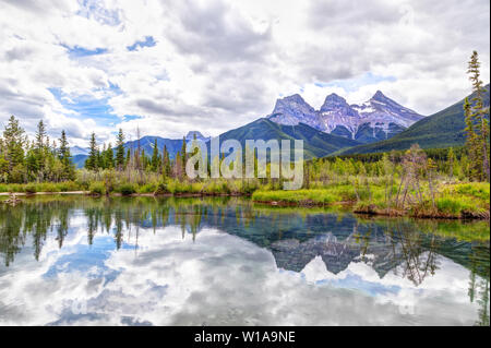 Die Canmore berühmten Three Sisters Berggipfel und deren Reflexionen auf dem Bow River im südlichen Banff Spektrum der Kanadischen Rockies an einem bewölkten S Stockfoto