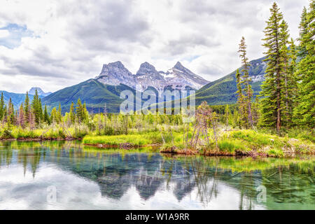 Die Canmore berühmten Three Sisters Berggipfel und deren Reflexionen auf dem Bow River im südlichen Banff Spektrum der Kanadischen Rockies an einem bewölkten S Stockfoto