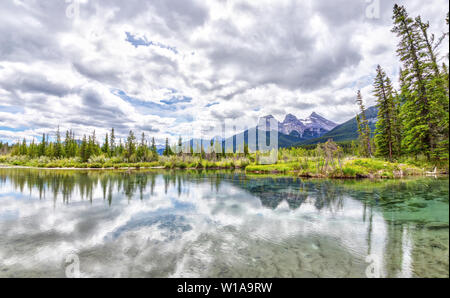 Weitwinkelaufnahme der Canmore berühmten Three Sisters Berggipfel und deren Reflexionen auf dem Bow River im südlichen Bereich des kanadischen Banff Ro Stockfoto